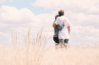 Couple Hugging in Grassy Field Under Blue Sky