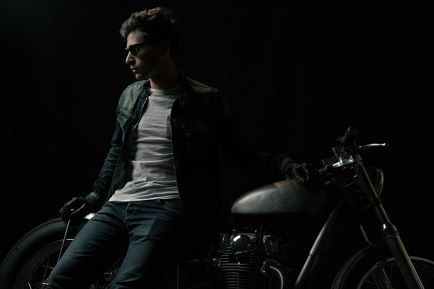 Man in Sunglasses Sitting on Vintage Motorcycle in Dark Studio