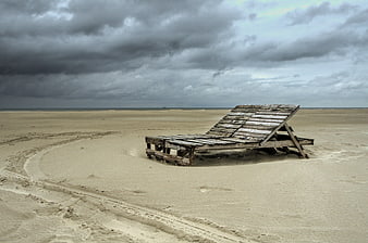 Weathered Wooden Beach Chair on Sandy Shore Under Stormy Sky