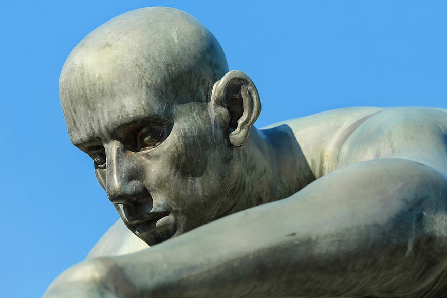 Close-up of bronze male athlete statue against blue sky