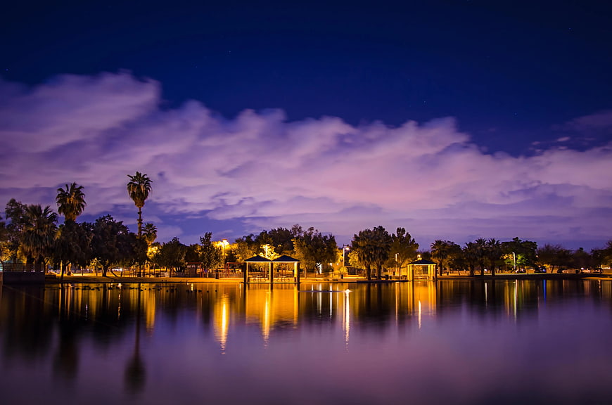 Night landscape of park lake with palm trees and purple clouds