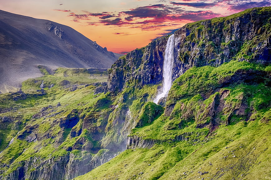 Dramatic waterfall cascading down green cliffs at sunset