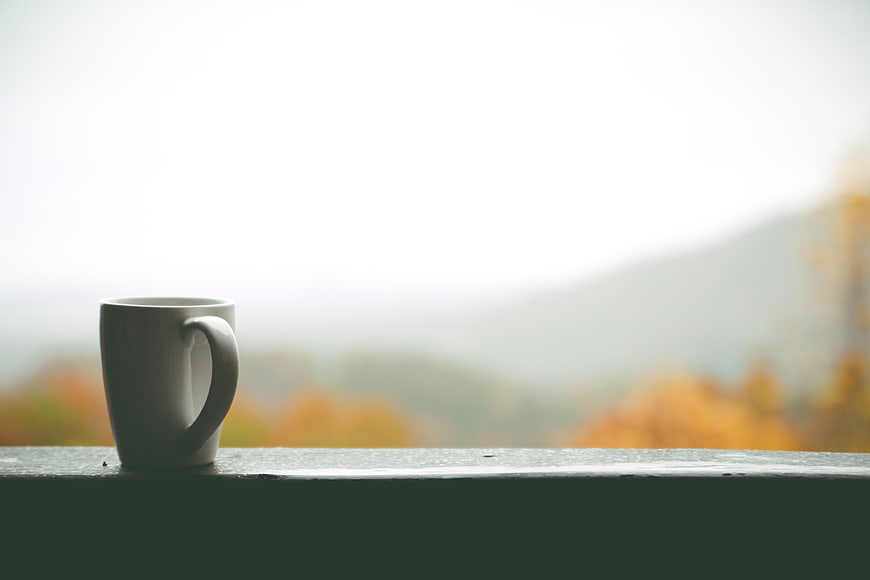 White Coffee Mug on Window Sill with Blurred Autumn Mountain View