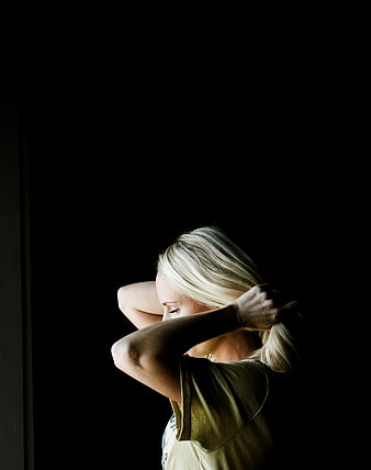 Blonde woman tying hair in dramatic low-key lighting