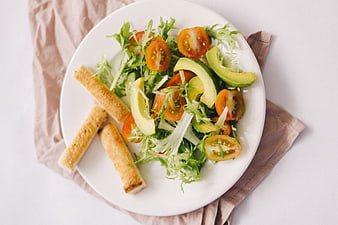 Fresh avocado and tomato salad with breadsticks on a white plate