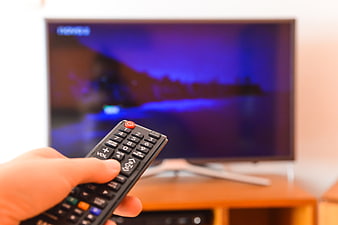 Hand holding remote control pointing at flat screen television
