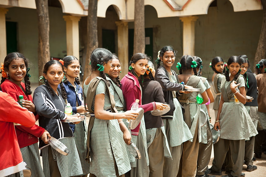 Schoolgirls in uniform waiting in line with plates