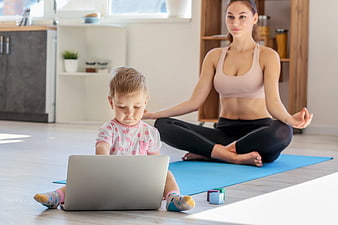 Mother doing yoga while child uses laptop at home