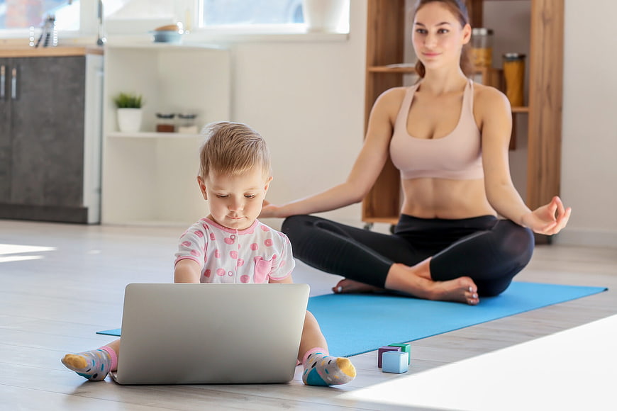 Mother doing yoga while child uses laptop at home