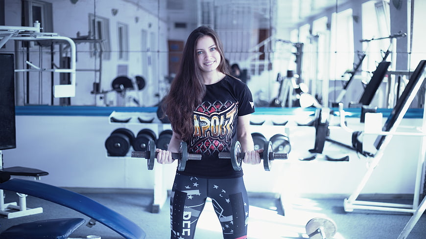 Smiling woman lifting dumbbells in gym