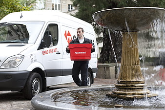 Courier driver carrying red Citytrans box near white van and fountain