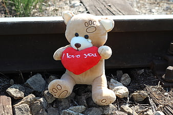 Teddy bear holding red heart on railway track