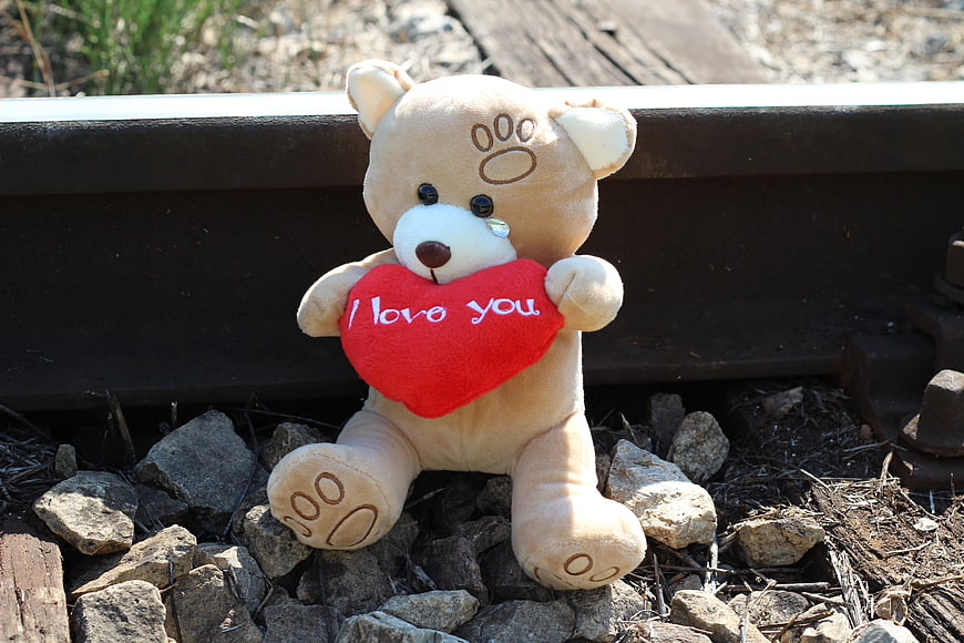 Teddy bear holding red heart on railway track