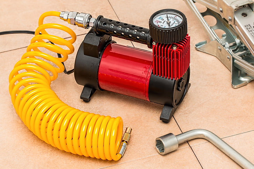 Red Portable Air Compressor With Yellow Coiled Hose On Tile Floor