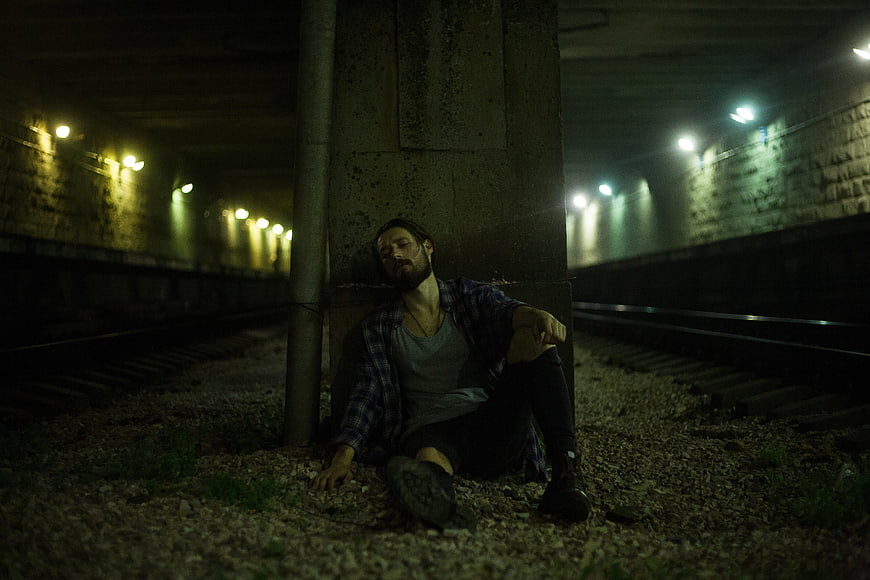 Tired man resting on railway tracks in dark tunnel