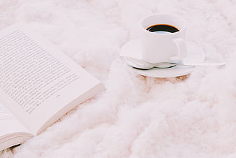 Cozy coffee cup and open book on fluffy white blanket