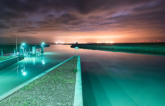 Long exposure night canal with teal lights and orange sky