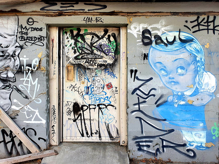 Urban Graffiti Wall with Blue Doll Mural and Tagged Door