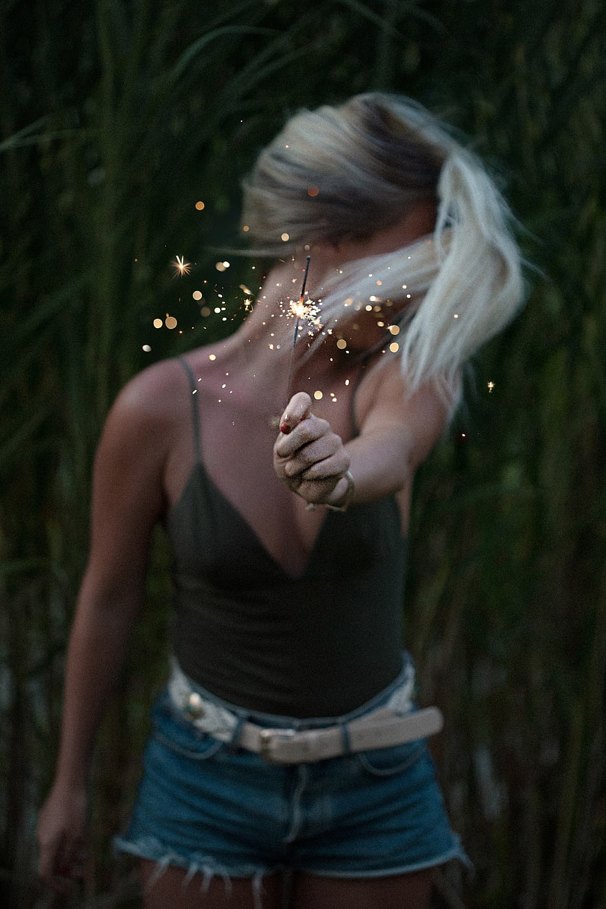 Woman holding sparkler in field at dusk