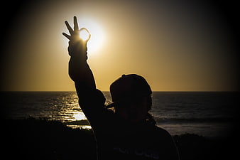 Silhouette of person making peace sign at sunset beach