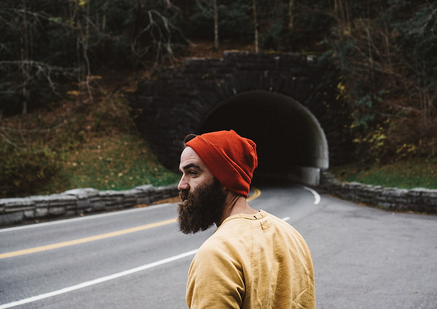 Bearded man in orange beanie standing on road near tunnel