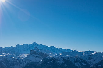 Snowy Mountain Peaks Under Bright Blue Sky with Sun Flare