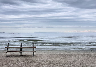 Empty wooden bench on sandy beach facing calm sea