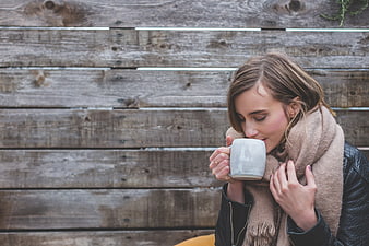 Woman drinking coffee against rustic wooden wall