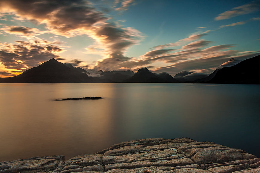 Serene Mountain Lake Sunset with Smooth Water and Rocky Foreground