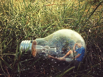 Man sitting inside a giant light bulb in a grassy field