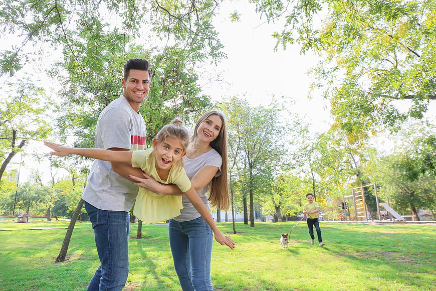 Happy family playing airplane game in park with dog