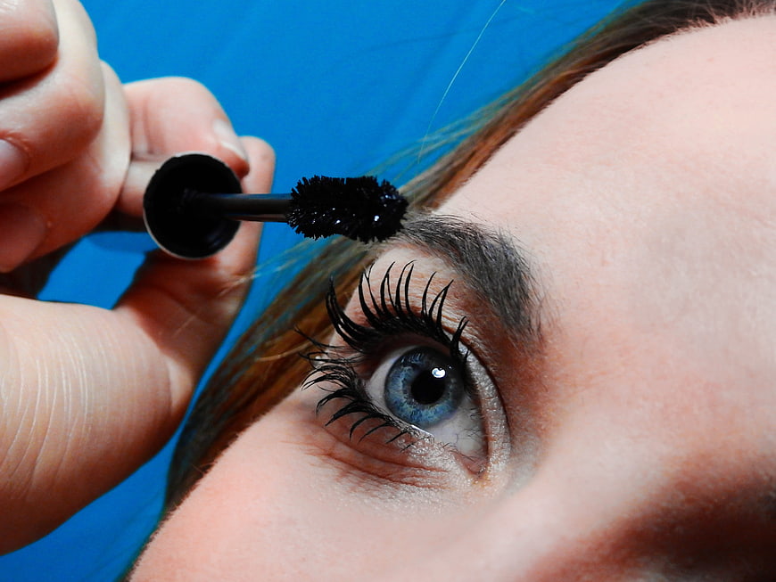 Close-up of woman applying mascara to blue eye