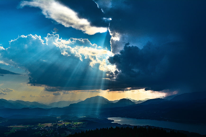 Dramatic Sunbeams Breaking Through Storm Clouds Over Mountain Lake Landscape