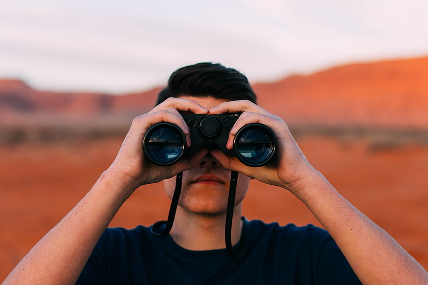 Man Looking Through Binoculars in Red Desert Landscape