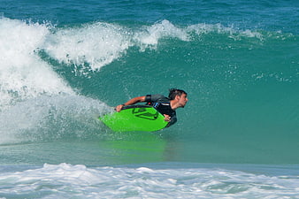 Man bodyboarding on a turquoise wave with green board