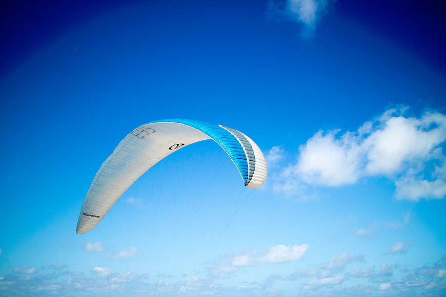 Blue and white paraglider soaring against a bright blue sky