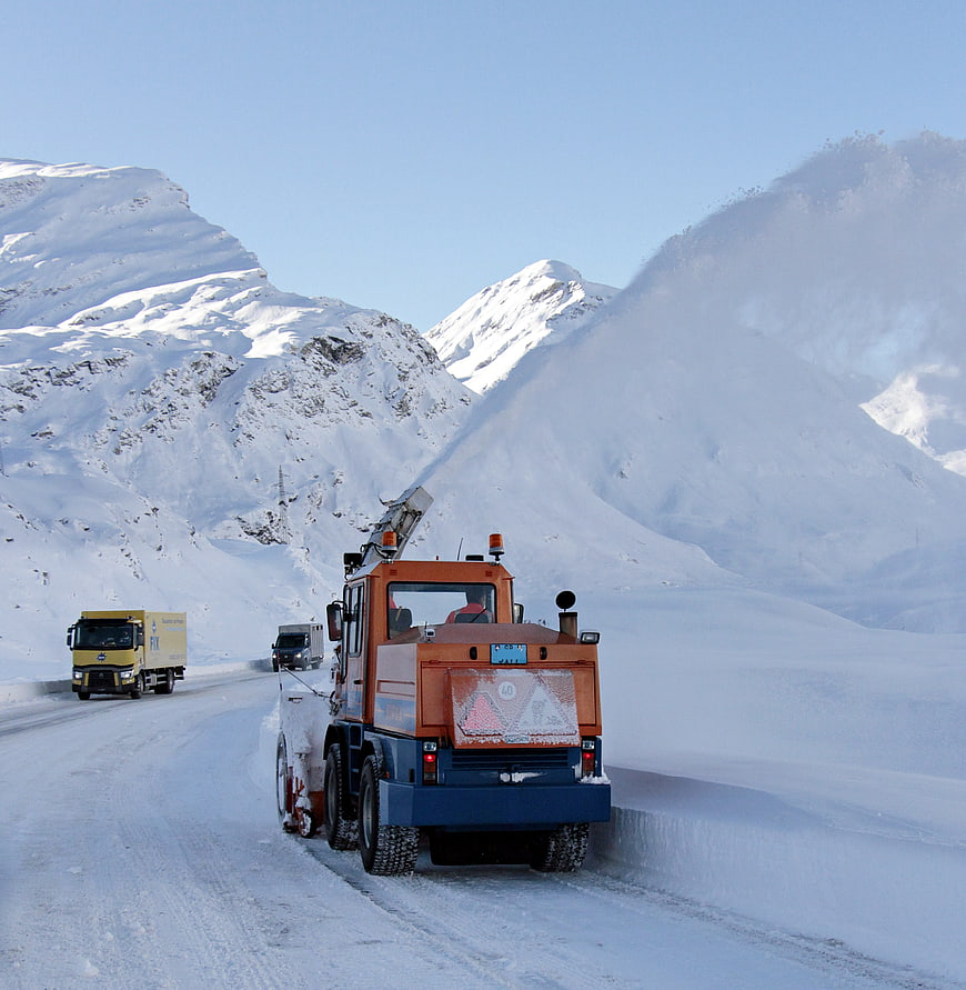 Snowplow clearing mountain road in winter landscape
