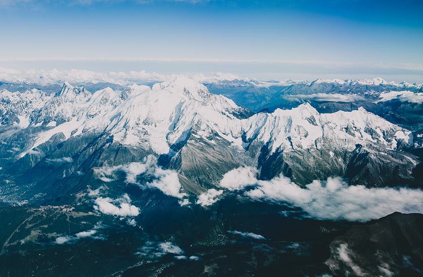 Aerial View of Snow-Capped Mountain Peaks Above Clouds