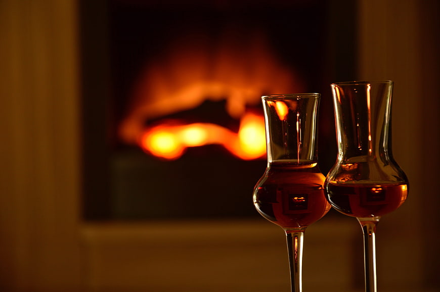 Two glasses of whiskey in front of a warm fireplace