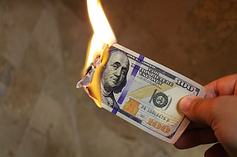 Hand holding burning hundred dollar bill prop