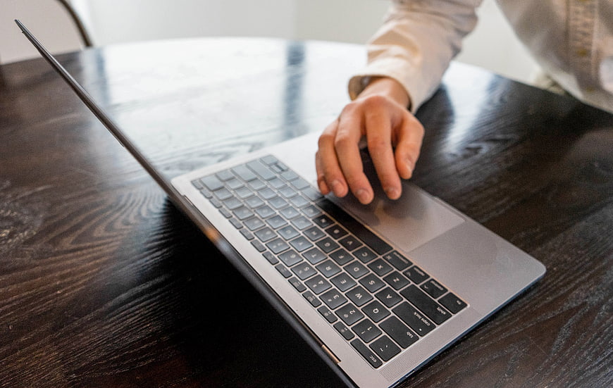 Close-up of hand using laptop trackpad on wooden desk