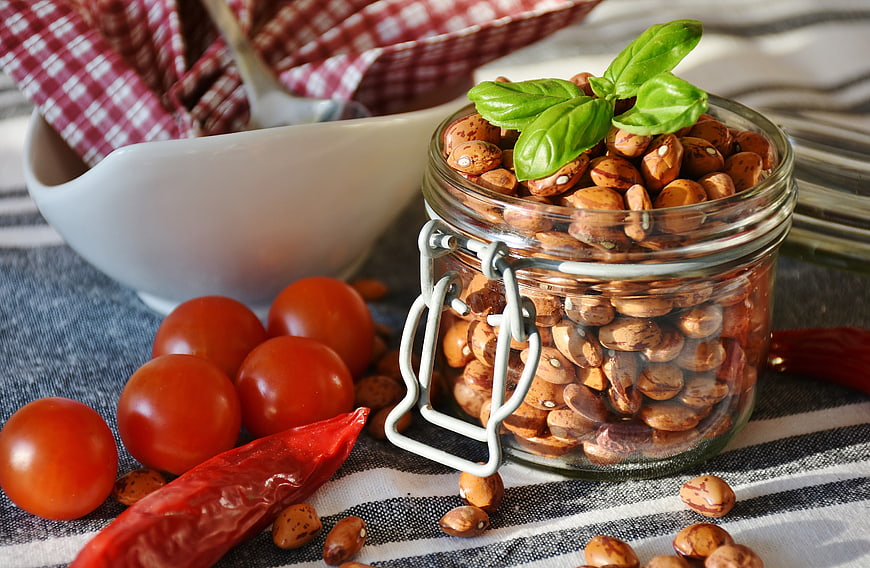 Glass jar of roasted beans with basil, cherry tomatoes, and dried chili pepper