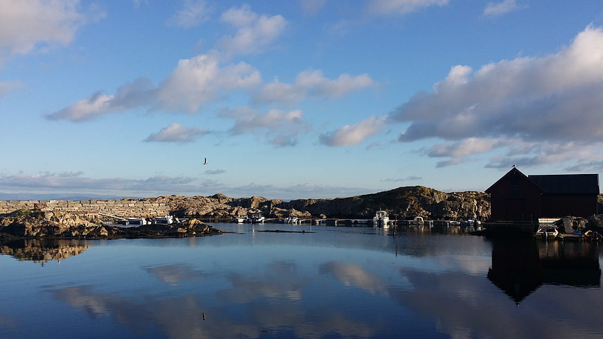 Serene Norwegian coastal village with red boathouse and calm water reflections