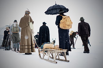 Historical reenactors in vintage winter clothing with sled and umbrella