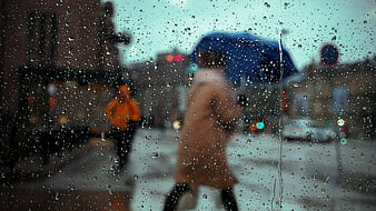 Raindrops on window with blurred city street and pedestrians