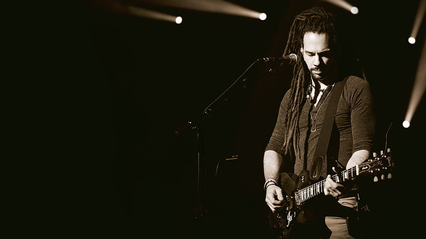 Male guitarist with dreadlocks performing on stage with spotlight