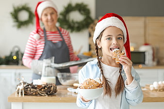 Happy girl eating gingerbread cookie with grandmother baking Christmas