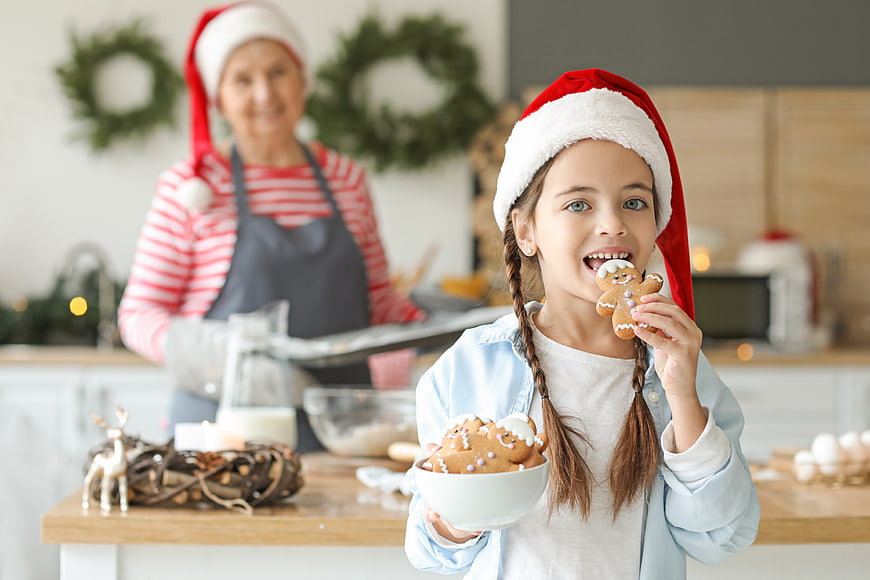 Happy girl eating gingerbread cookie with grandmother baking Christmas