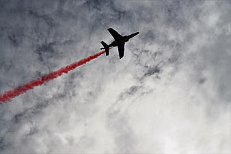Silhouette of Jet Fighter with Red Smoke Trail in Cloudy Sky