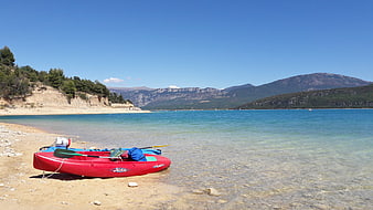 Red Kayak on Sandy Beach with Turquoise Sea and Mountains